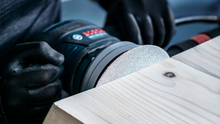 佩戴安全设备的人员使用电动工具打磨木质表面。