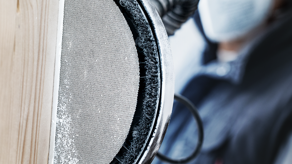 一名佩戴安全设备的人员正在使用电动工具打磨木质表面。