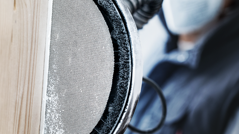 一名佩戴安全设备的人员正在使用电动工具打磨木质表面。