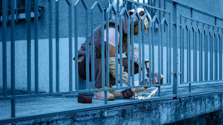 佩戴安全设备的人员使用电动工具切割金属栅栏。