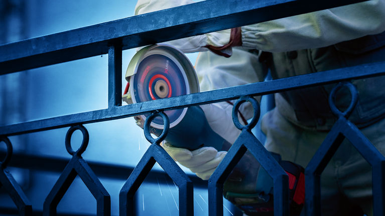 一名佩戴安全设备的人正在用电动工具磨削金属栅栏。