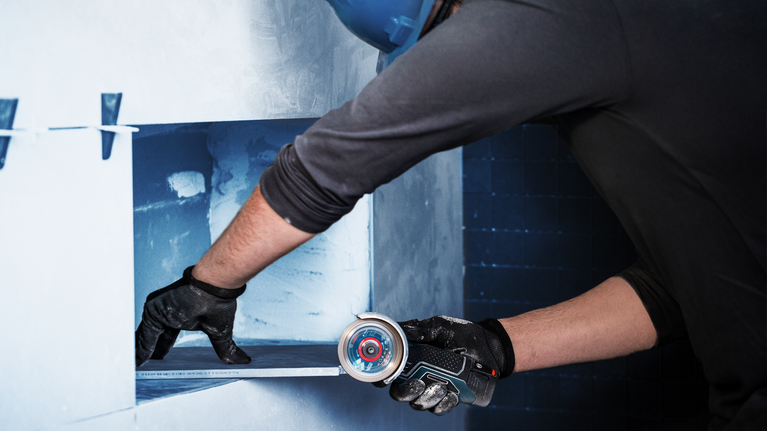 一名佩戴安全设备的人员使用小型电动工具在墙上开孔。