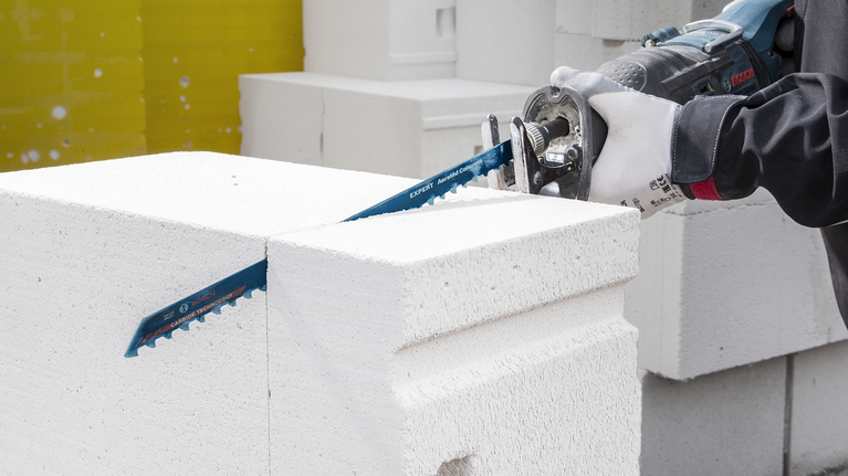 佩戴安全设备的人员用往复锯切割白色混凝土块。