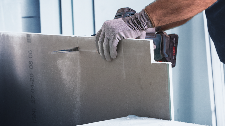 佩戴安全设备的人员使用电动工具切割干墙。