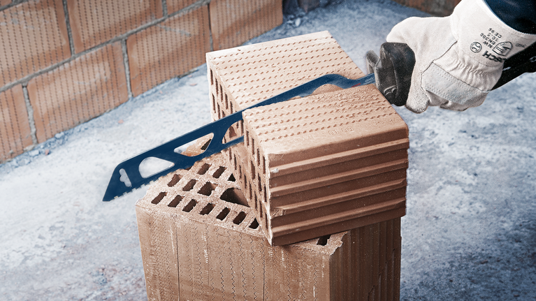 佩戴安全设备的人员用手锯切割砖块。