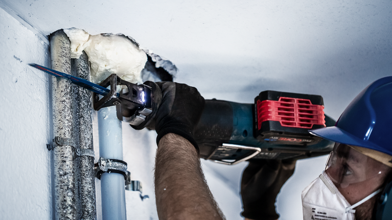 一名佩戴安全设备的人员使用往复锯切割金属管道。