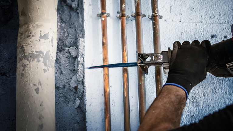 一个人用往复锯切割安装在墙上的铜管。