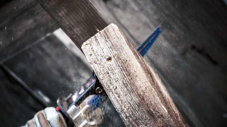 佩戴安全设备的人员用往复锯切割木板。