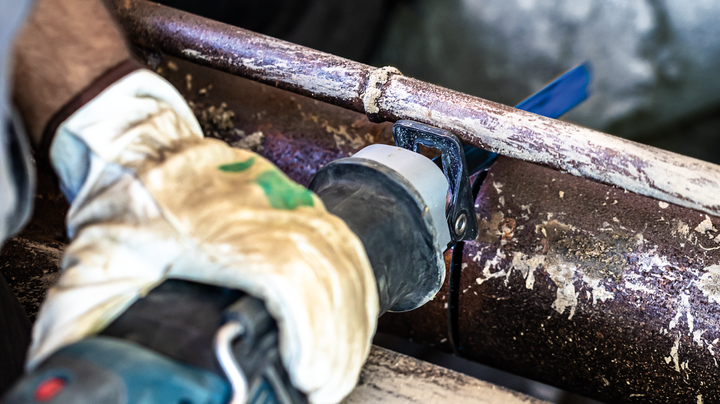 一名佩戴安全设备的人用往复锯切割生锈的金属管。