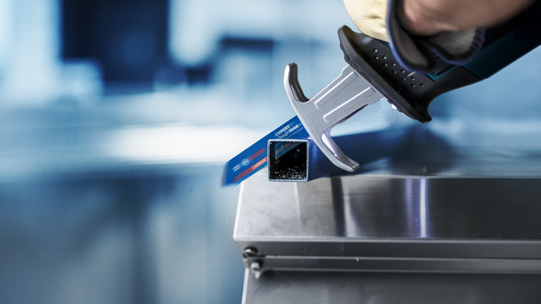 佩戴安全设备的人员使用往复锯切割金属管。