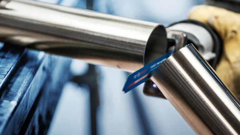 佩戴安全设备的人员用往复锯切割金属管。