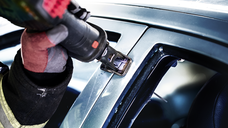 一名佩戴安全设备的人员使用电动工具切割汽车窗框。