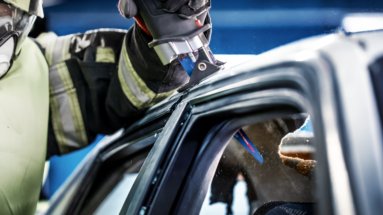 一名佩戴安全设备的人使用往复锯切割汽车车顶。