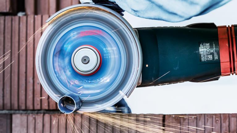 一名佩戴安全设备的人员正在使用旋转角磨机切割金属管道。