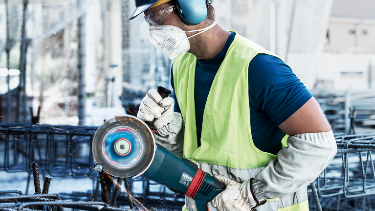 一名佩戴安全设备的人用电动工具研磨金属钢筋，产生火花。