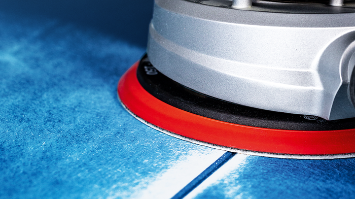 带有红色底座的电动工具正在打磨蓝色表面。