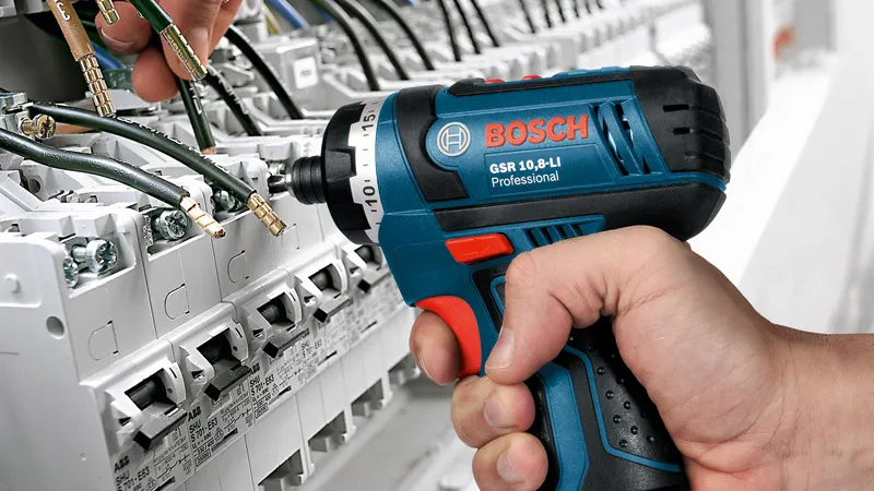 一个人使用无绳电钻来固定配电盘上的电线。