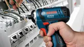 一个人使用无绳电钻来固定配电盘上的电线。