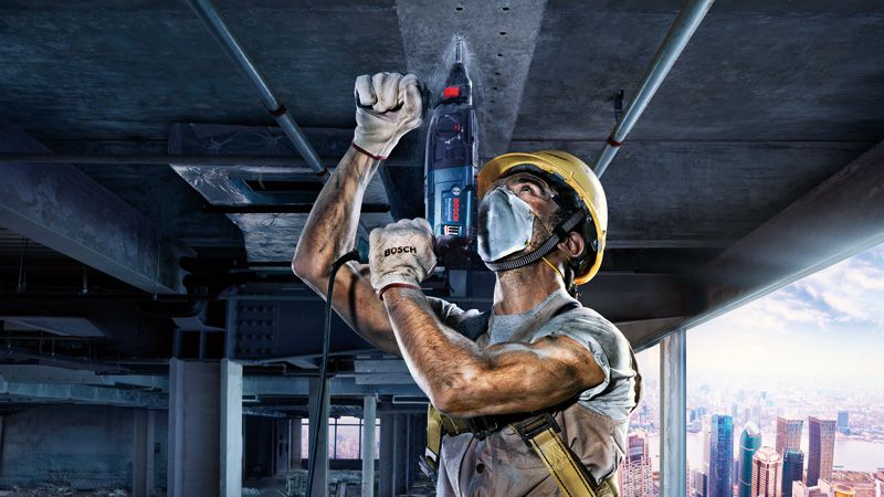 一名佩戴安全设备的人员在建筑工地的混凝土天花板上钻孔。.