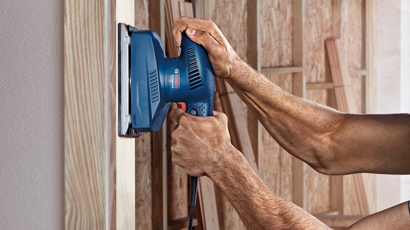 一名工人正在用轨道式砂光机打磨木质表面。