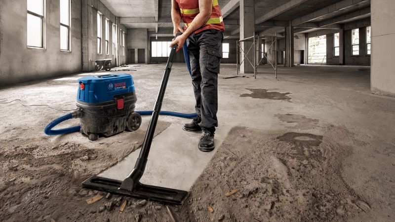 一名佩戴安全设备的人员正在一栋未完工的大型建筑物内吸尘混凝土灰尘。.