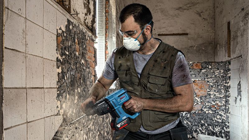 一名佩戴安全设备的人员使用电动工具从墙上拆除瓷砖。.