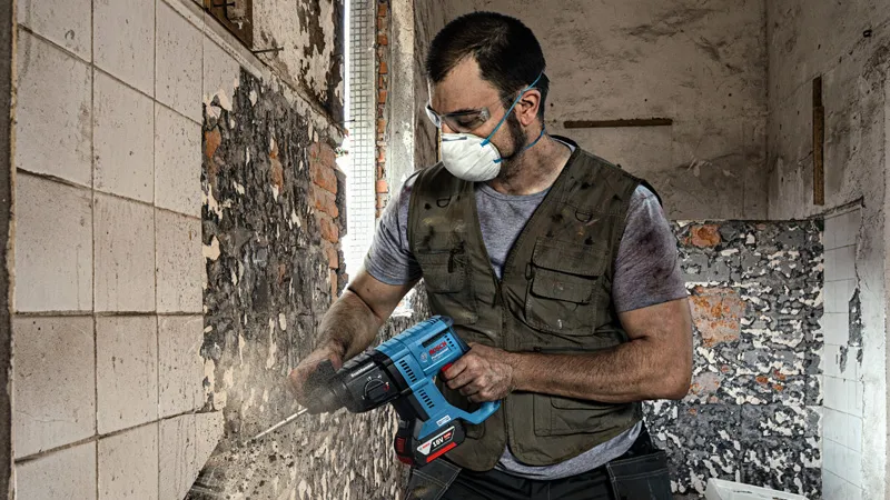 一名佩戴安全设备的人员使用电动工具从墙上拆除瓷砖。.