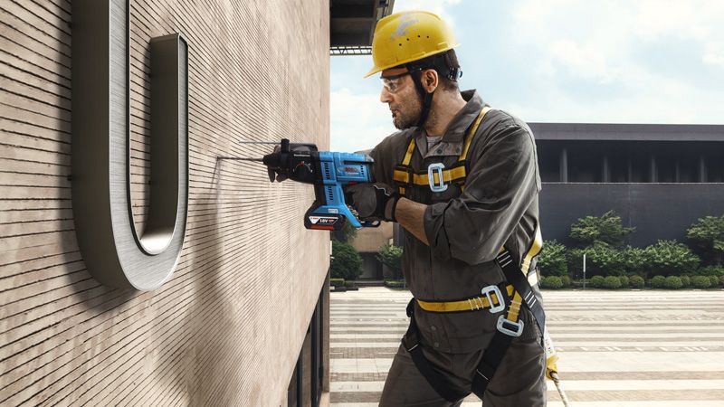 一名佩戴安全设备的人员悬空钻入建筑物墙壁。.