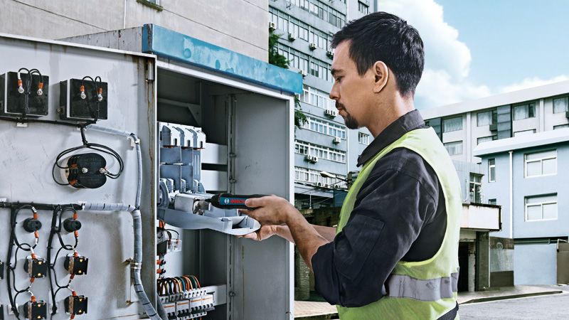 一名佩戴安全设备的人员正在使用无绳螺丝刀操作电气面板。.