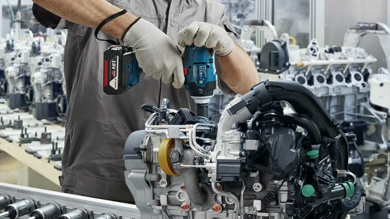 一名佩戴安全设备的人员使用无绳冲击扳手修理发动机组件。.