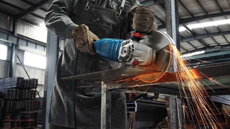 一名佩戴安全设备的人用大型角磨机切割金属板，火花四溅。.