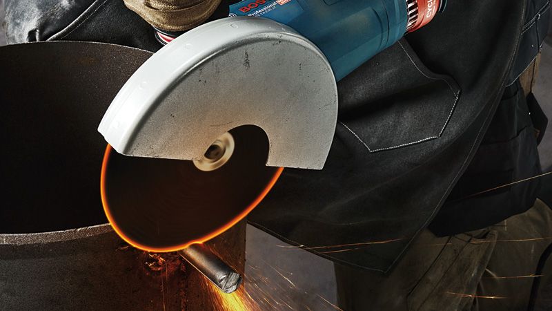 一名佩戴安全设备的人员使用手持角磨机切割金属管道。.
