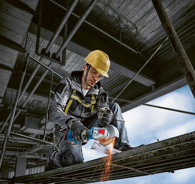 一名佩戴安全设备的人使用无绳角磨机切割金属。.