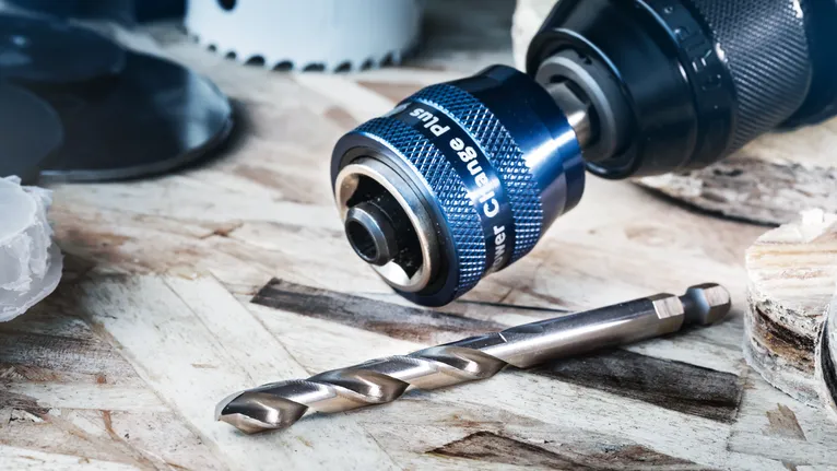 木质表面上带有金属钻头的钻夹头附件的特写。