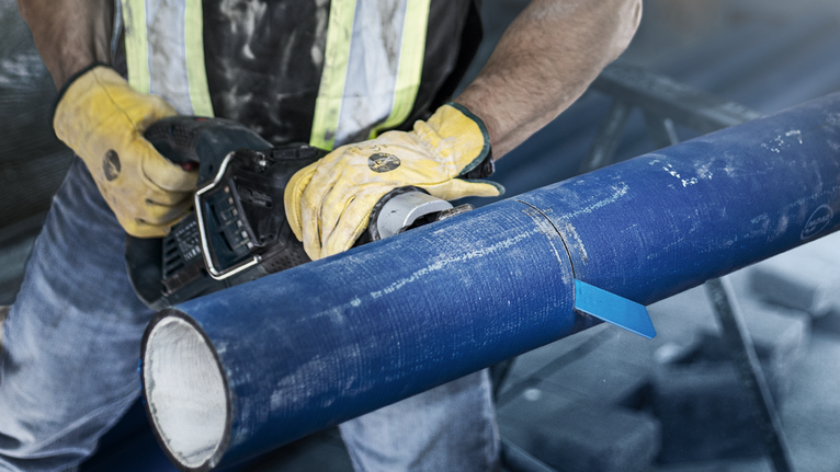 佩戴安全设备的人员使用电动工具切割一根蓝色的大管道。