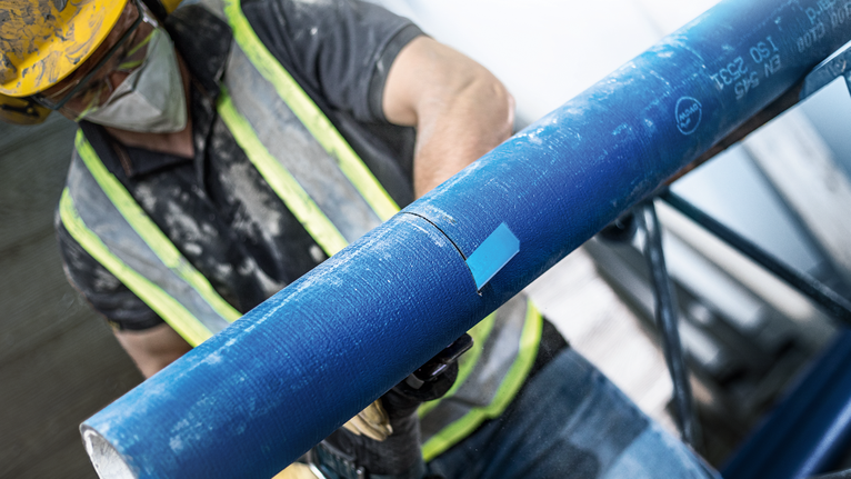 佩戴安全设备的人员使用电动工具切割蓝色管道。