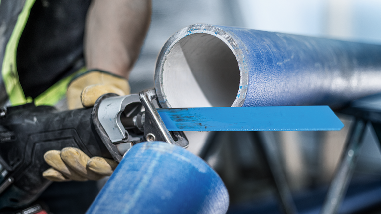 佩戴安全设备的人员使用往复锯切割一根蓝色大管子。