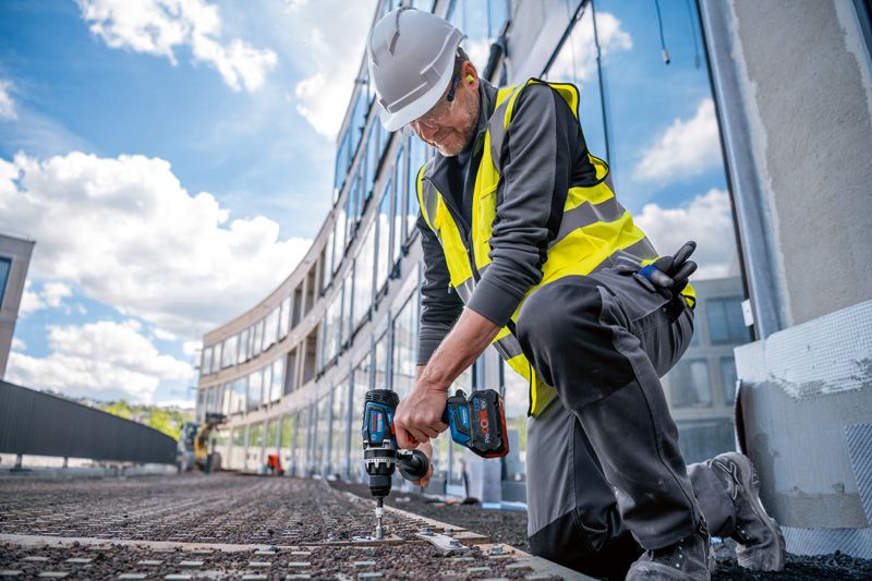 一名佩戴安全设备的人员在施工现场使用无绳电钻。.