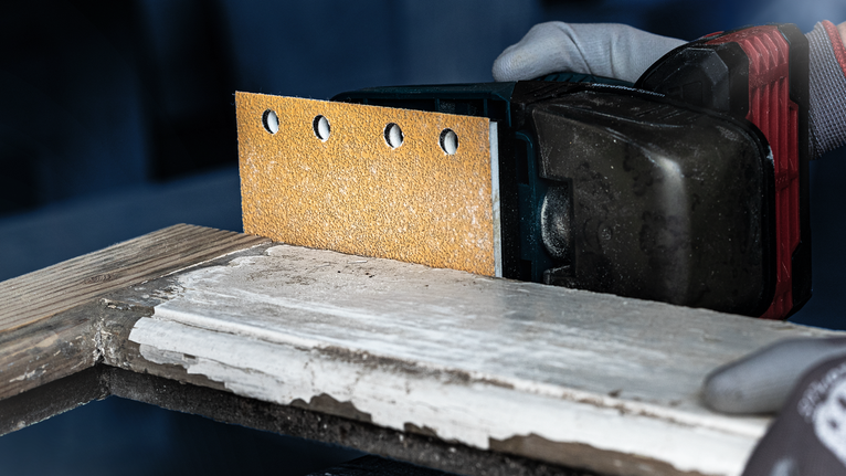 一名佩戴安全设备的人员使用无绳电动砂光机打磨木材。