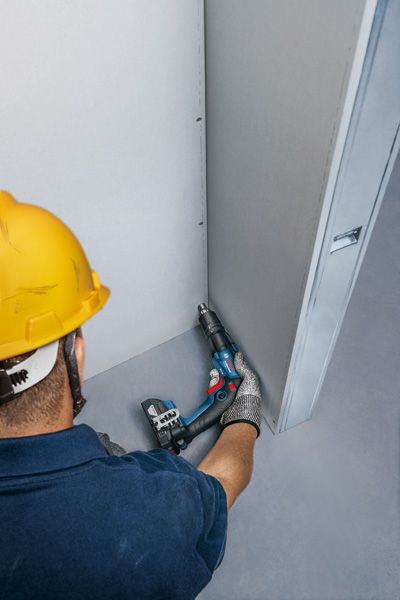 一名佩戴安全设备的人员正在用无绳螺丝刀固定干墙。.