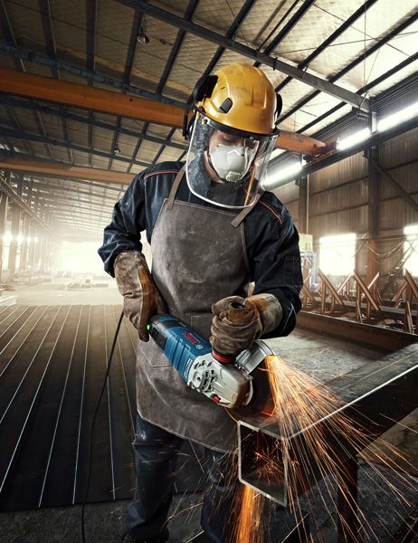 工厂里，一名佩戴安全设备的工人正在研磨金属，产生明亮的火花。.