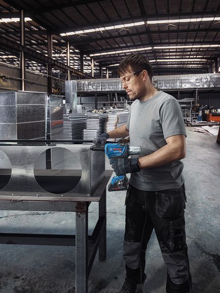 一名佩戴安全设备的人员在工厂的金属通风管道上钻孔。.