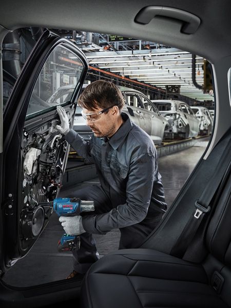 在汽车工厂里，一名佩戴安全设备的人员使用电动工具组装车门。