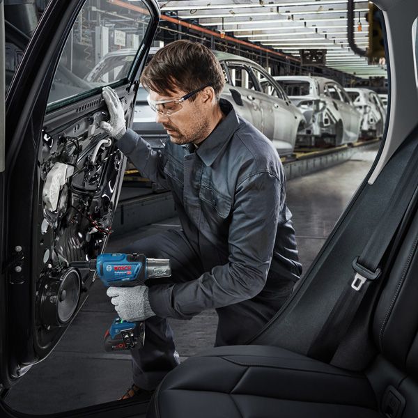 一名佩戴安全设备的人员在工厂里使用电动工具组装车门。