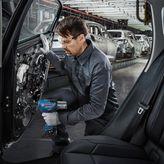 一名佩戴安全设备的人员在工厂里使用电动工具组装车门。