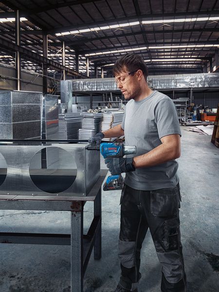 一名佩戴安全设备的人员使用无绳铆钉枪固定金属管道。.