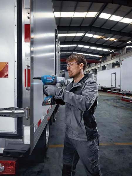 一名佩戴安全设备的人员使用无绳铆钉枪紧固卡车车门。.