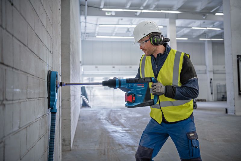 一名佩戴安全设备的人员使用无绳旋转锤在混凝土墙上钻孔。.