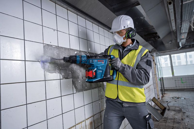 一名佩戴安全装备的人员使用无绳旋转锤敲碎墙砖。