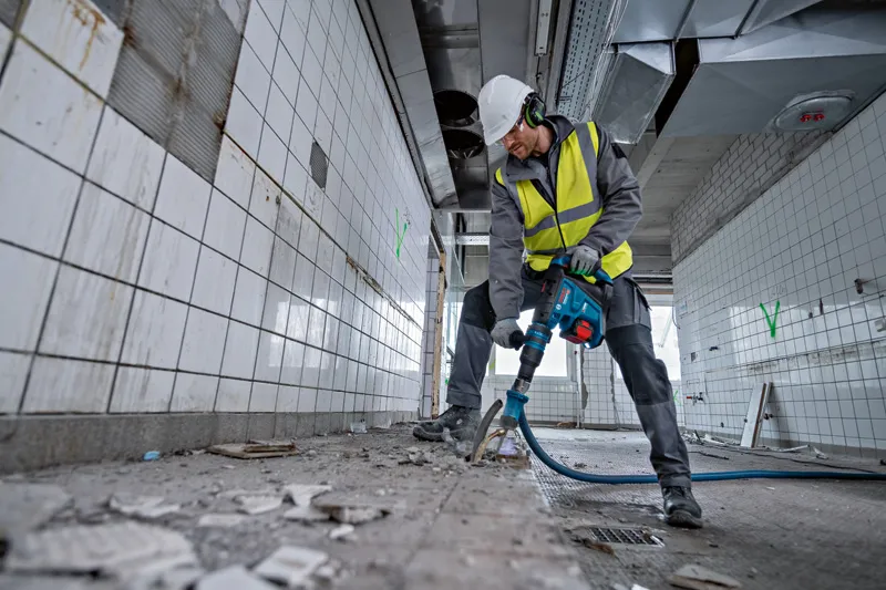 一名佩戴安全装备的人员使用旋转锤敲碎瓷砖房间里的地砖。